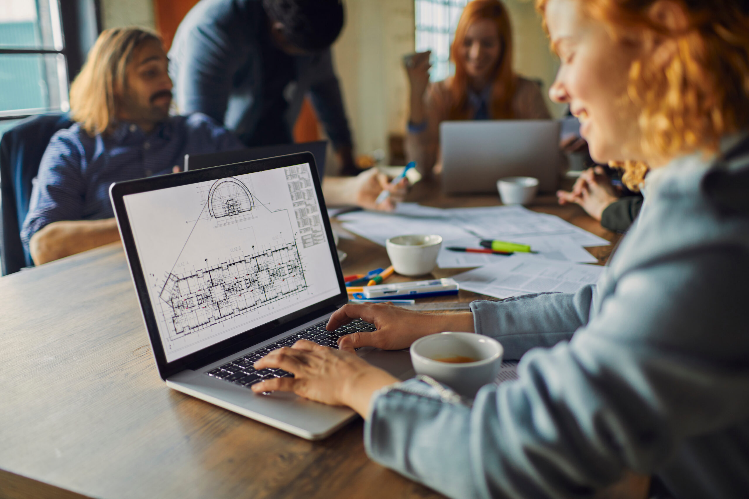 Team collaborating with laptop and blueprints. Team collaborating with laptop and blueprints.